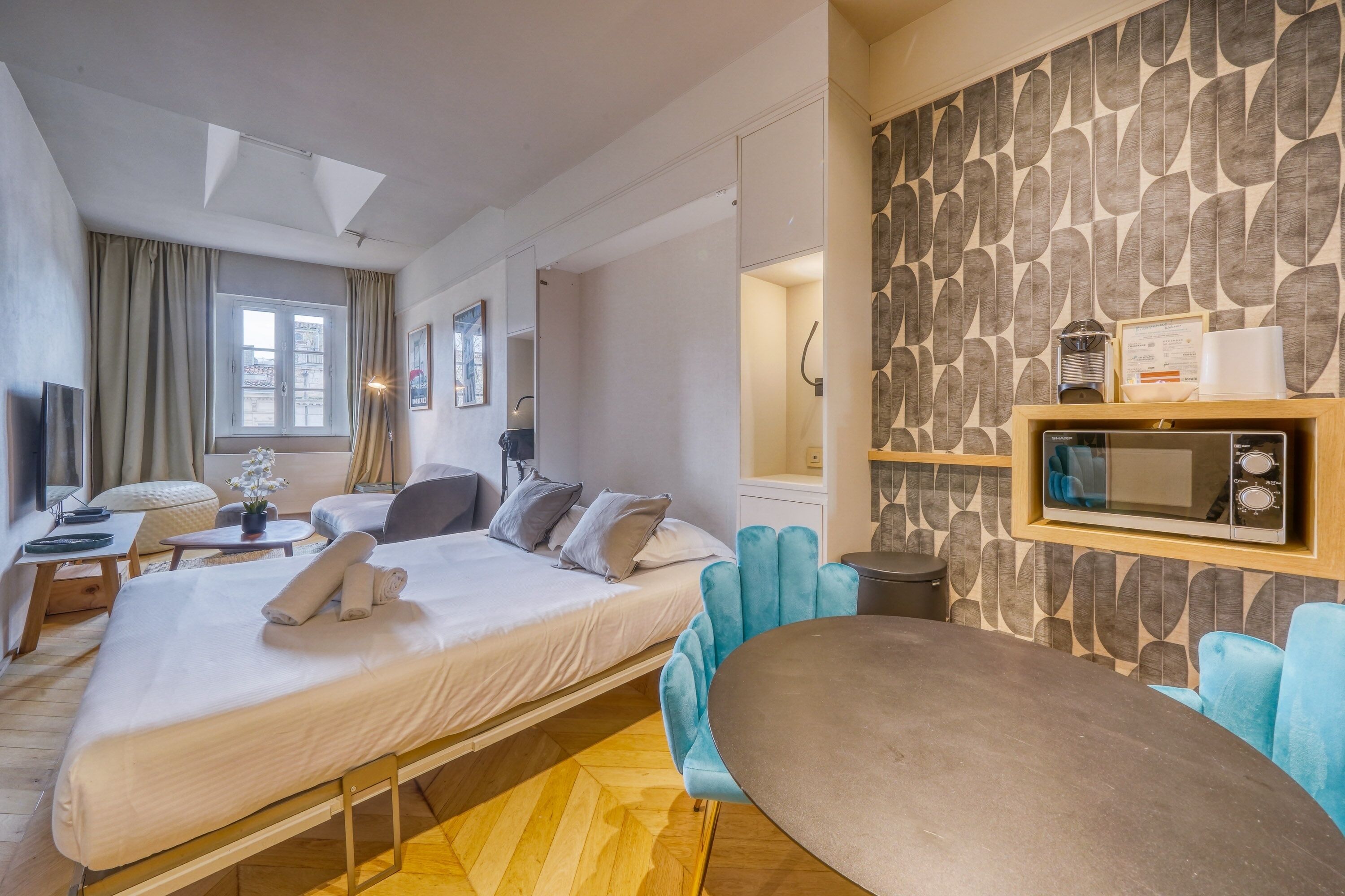 A modern hotel room with a bed, a desk, a chair, a sofa, and a microwave on the wall.