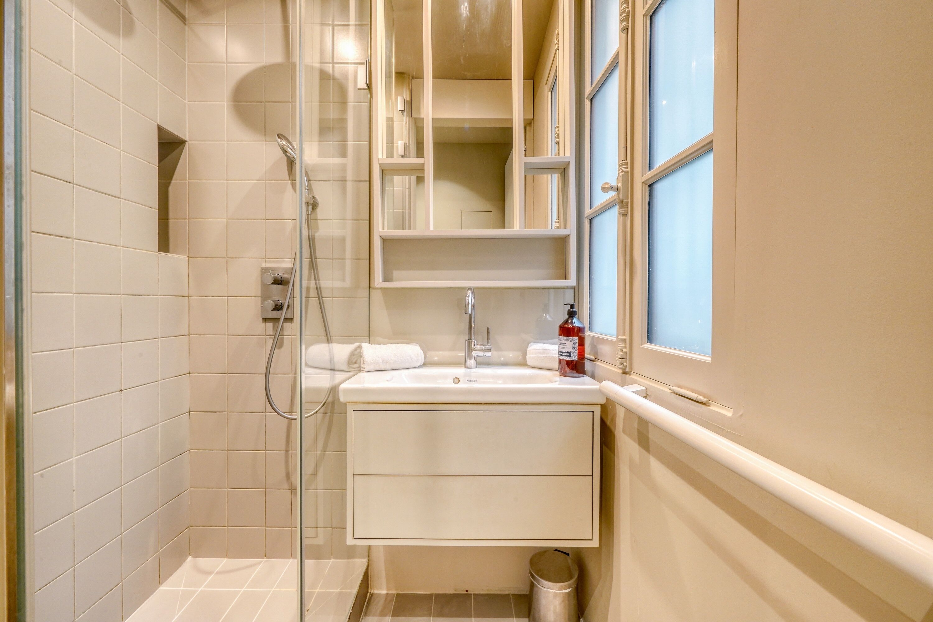 Een badkamer met een douche, een wastafel met spiegel en een raam.