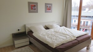 Ein Schlafzimmer mit einem Bett, Nachttischen, einem Fenster und Blick auf Gebäude.