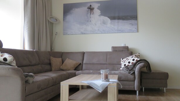 Ein Wohnzimmer mit einem beigefarbenen Sofa, einem kleinen Holztisch und einem Gemälde eines Leuchtturms an der Wand.