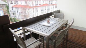 Ein Balkon mit einem Holztisch und vier Korbstühlen, mit Blick auf ein Wohngebiet mit roten Dächern.