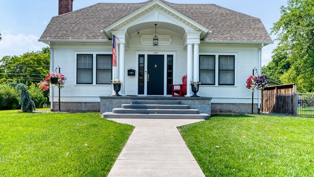 A two-story house with a front porch, a flag, and steps leading to the door.