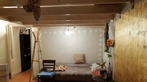 A bedroom with a bed, a chair, a small table, a fan, and a window with curtains. - La casa di Daniele (Brescia)