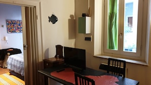 A room with a bed, a desk, a chair, a window with green curtains, a wall clock, and a small fish decoration. - La casa di Daniele (Brescia)