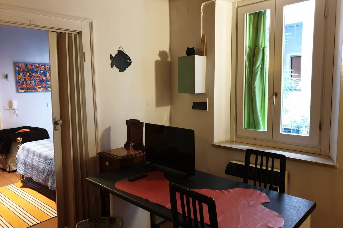 Une pièce comprenant un lit, un bureau, une chaise, une fenêtre avec des rideaux verts, une horloge murale et une petite décoration représentant un poisson.