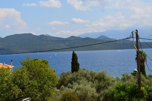 Paisaje costero con vista despejada al mar, montañas a lo lejos y una línea eléctrica en primer plano.