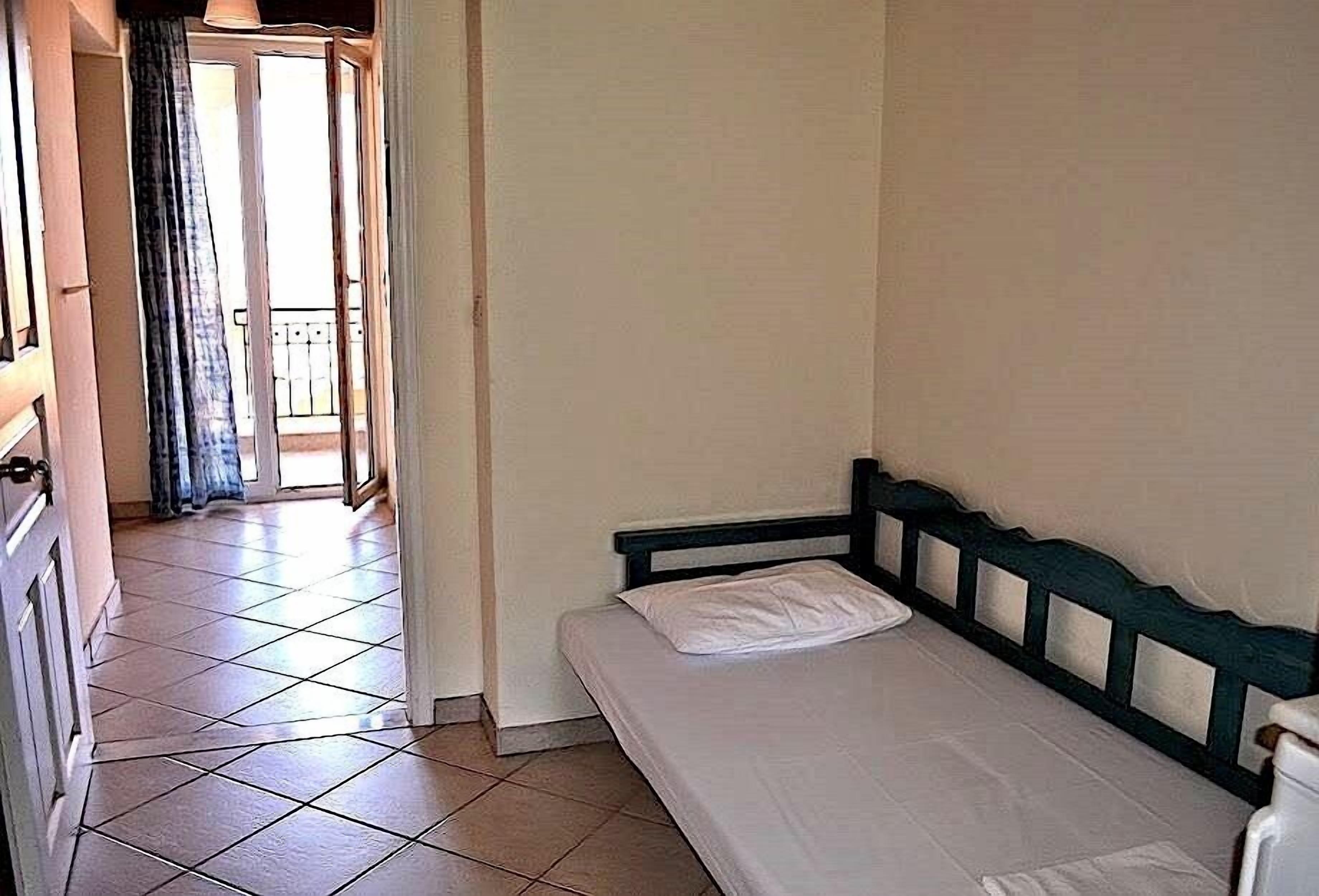A bedroom with a single bed, a door leading to a balcony, and tiled flooring.