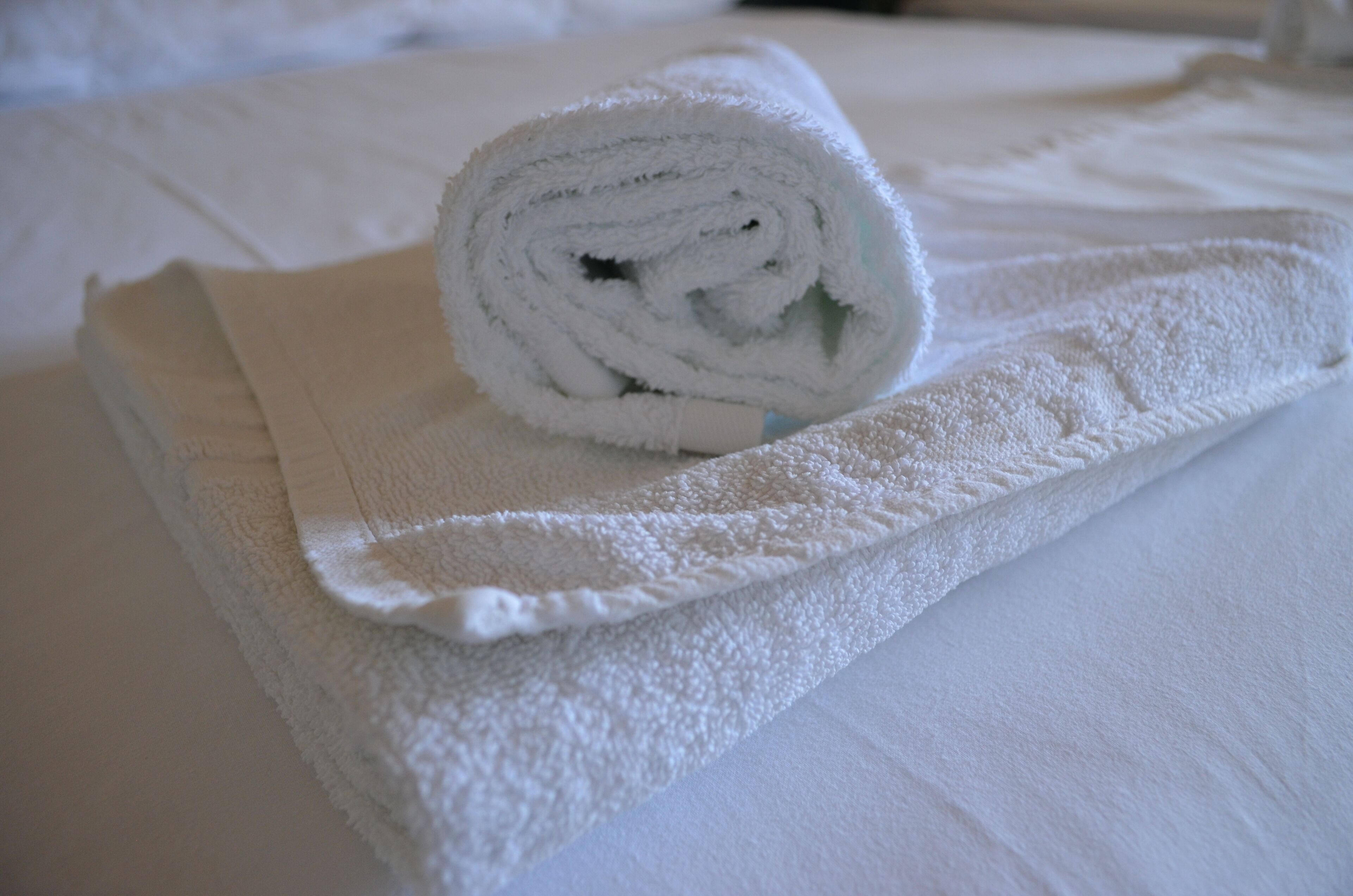 A neatly folded white towel on a bed with a white pillow.