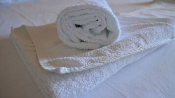 A neatly folded white towel on a bed with a white pillow.
