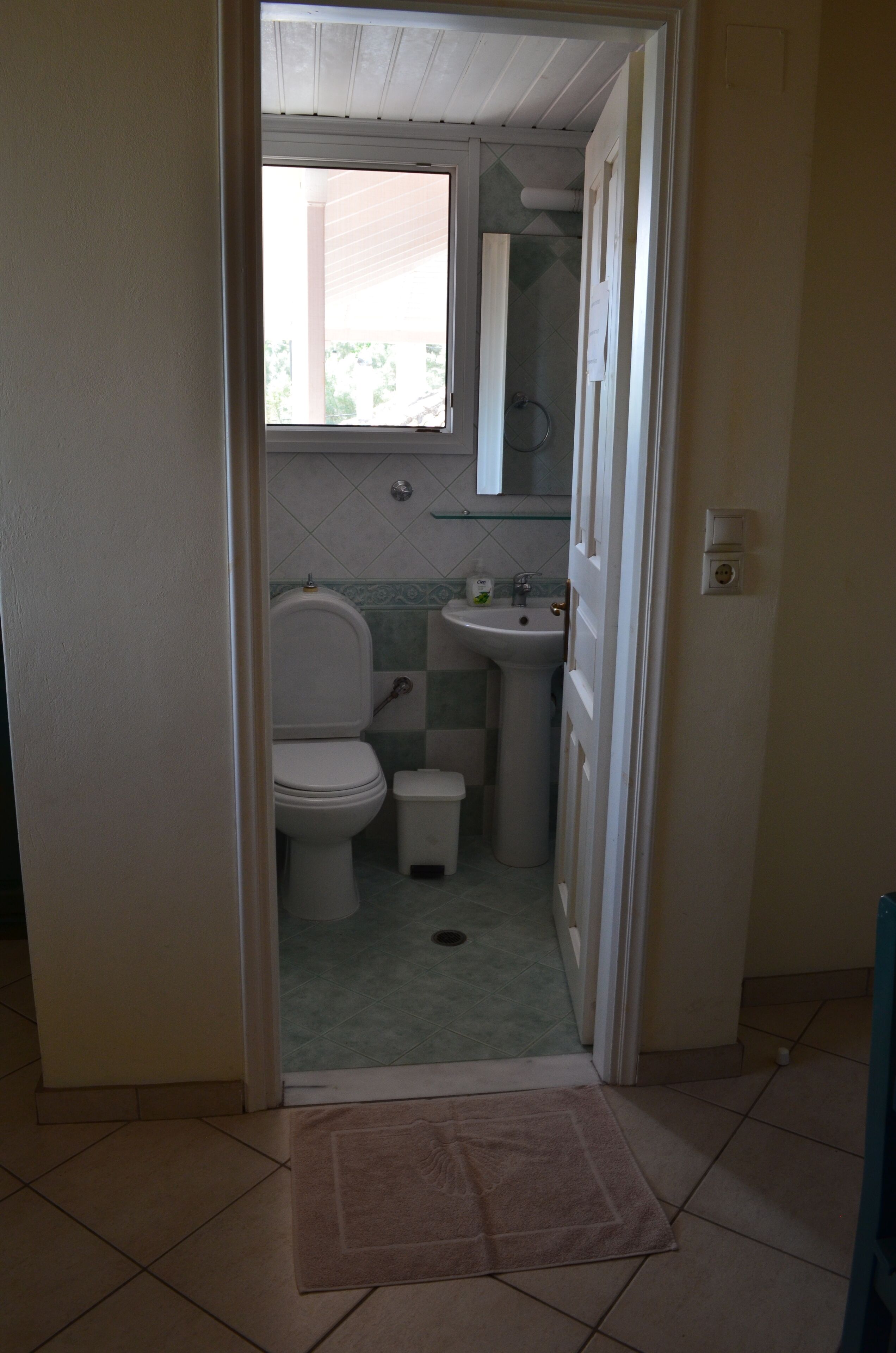 A small bathroom with a toilet, sink, and a window above the sink.