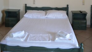 Una cama bien hecha con sábanas y toallas blancas, cabecera de madera y dos mesitas de noche con lámparas.