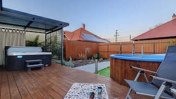 A wooden deck with a hot tub, a covered seating area, and a fenced garden.