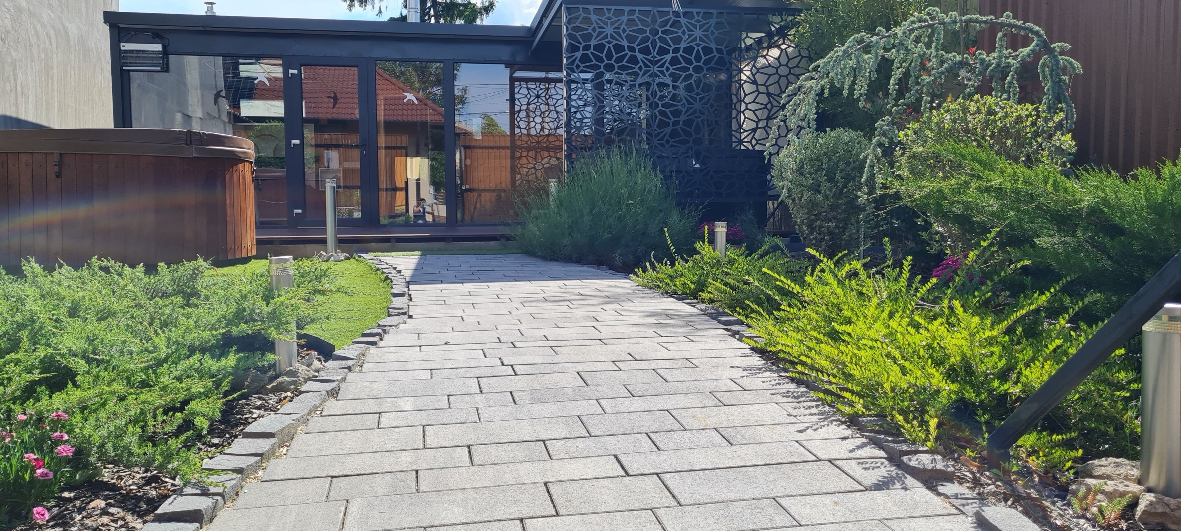 Un chemin pavé mène à un bâtiment moderne doté de grandes fenêtres et d’une structure décorative en treillis.