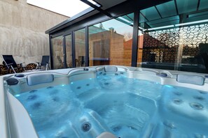 Un jacuzzi con cerramiento de vidrio, cerca de madera y cielo despejado.