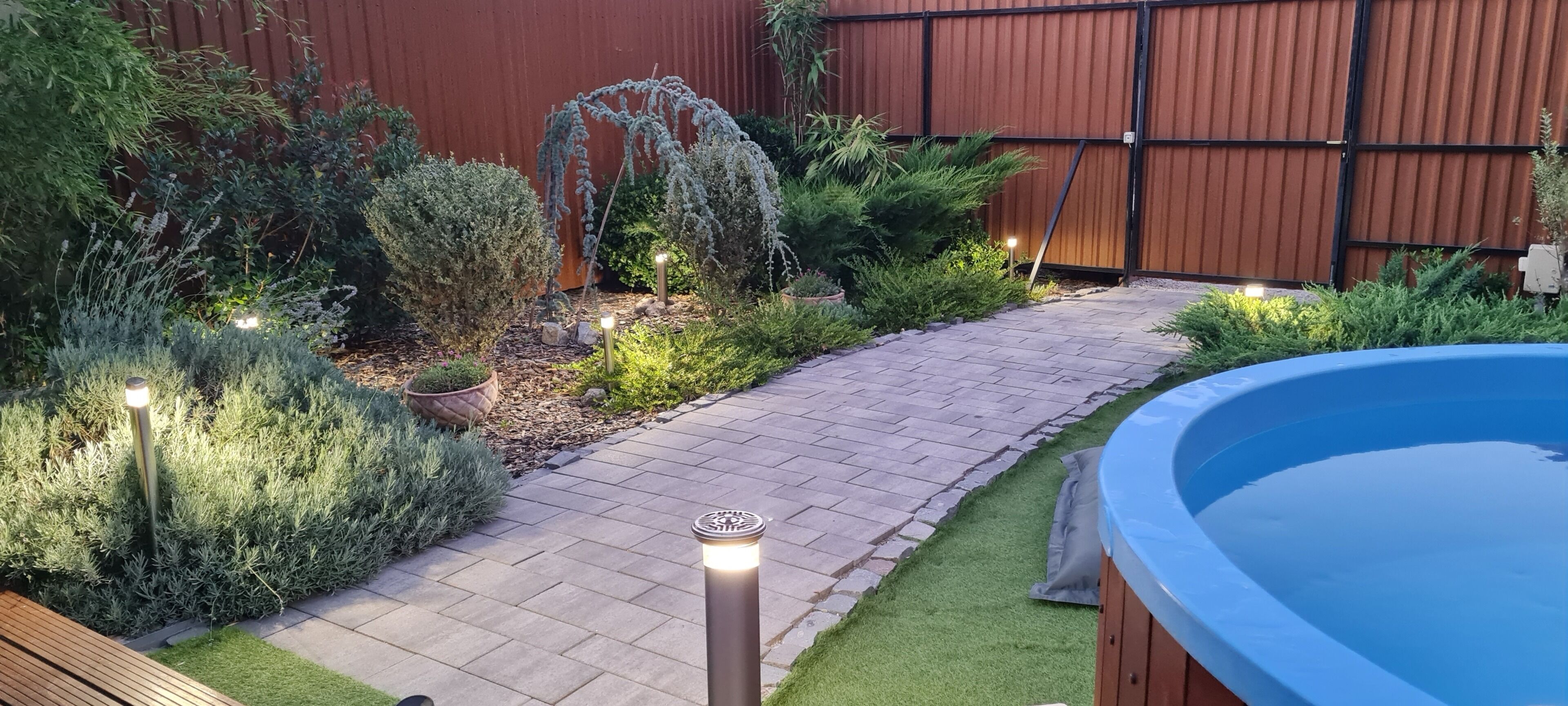 Un jardin avec un chemin dallé, une piscine et diverses plantes.