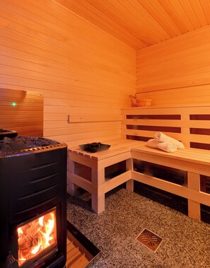 A sauna room with a wood-burning stove, benches, and a towel on one of the benches. - Anita Apartments a Modern Riverside Boutique Hotel (XXI. kerület)