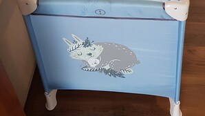 Una bañera azul para bebés con un diseño de animal de caricatura, ubicada en una habitación con piso de madera y una ventana con persianas verticales.