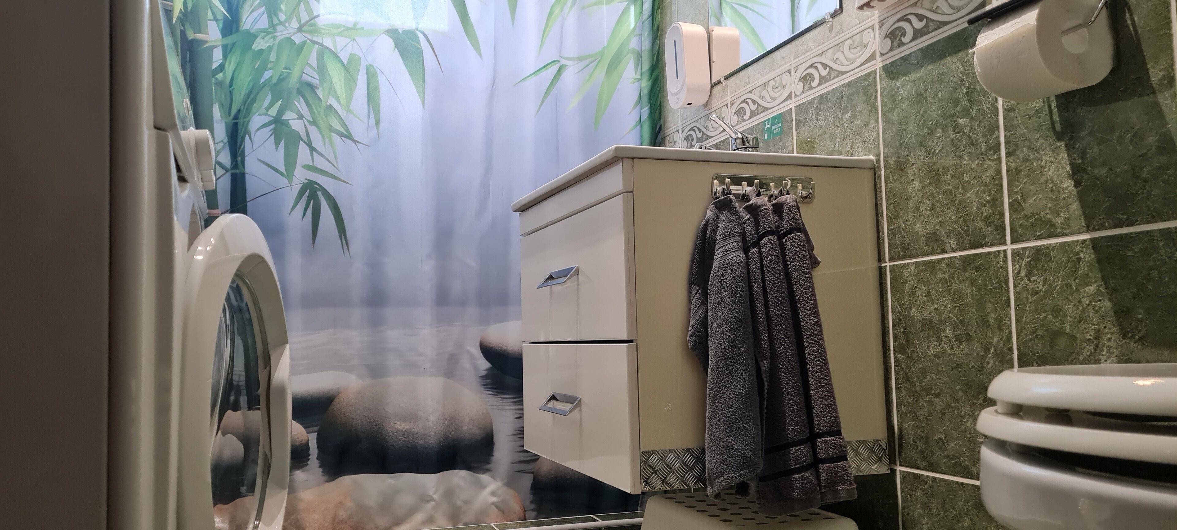 A bathroom with a toilet, a sink, a towel rack, and a shower curtain with a bamboo leaf design.