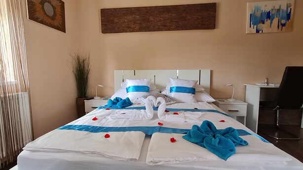 Una cama bien hecha con ropa de cama azul y blanca, una silla, un escritorio y una planta en una habitación de hotel.