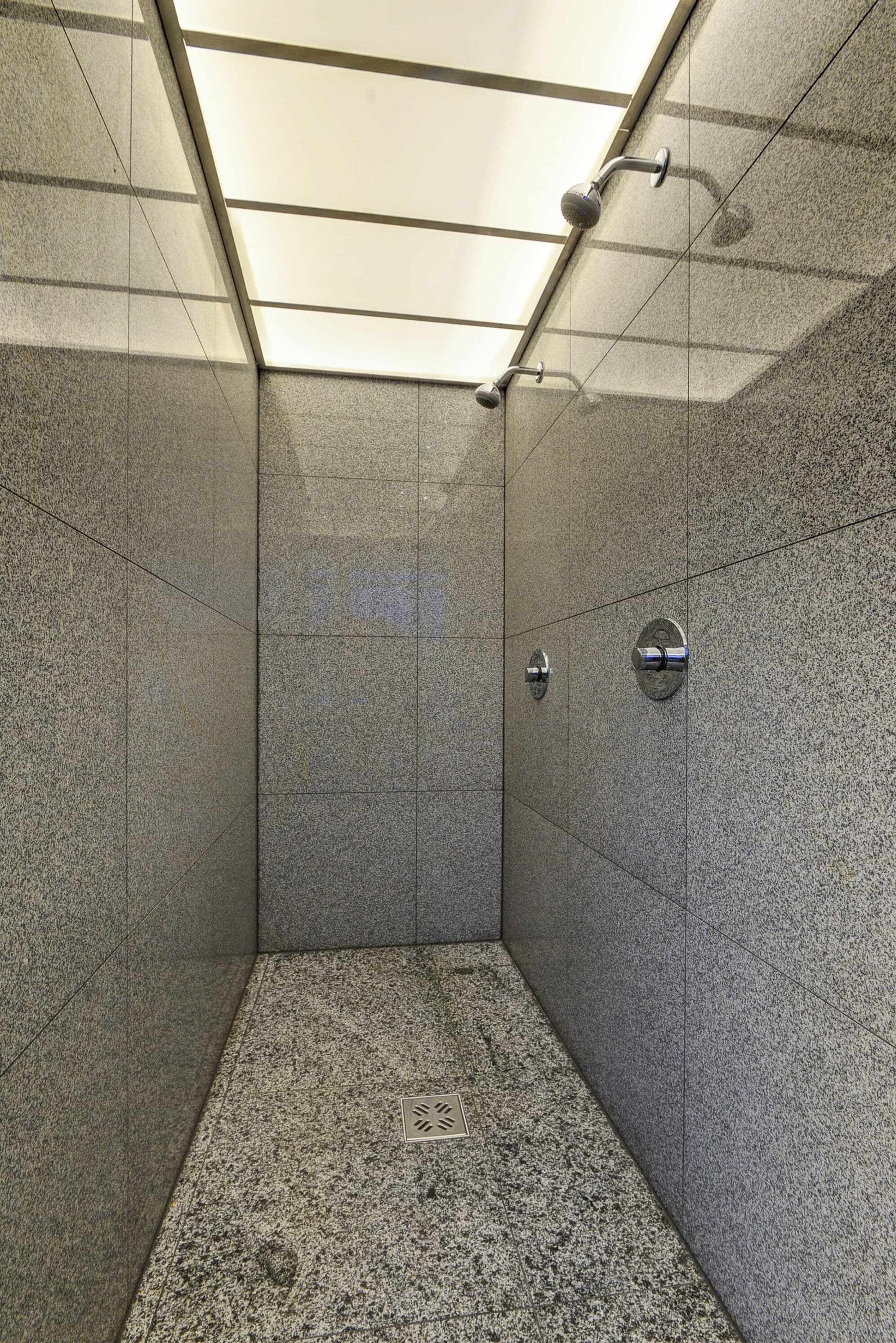Eine Dusche mit Glasabtrennung, Duschkopf zum Handgebrauch und am Wand befestigtem Wasserhahn.