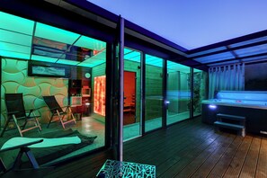Un espacio exterior moderno con una bañera de hidromasaje, asientos y un ventanal que da a una habitación.