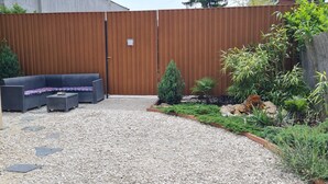 Un patio con cerramiento de madera, un área de estar y un jardín con plantas y rocas.