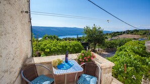 A balcony with a table and chairs, overlooking a vineyard and a body of water. - Apartment Marija (Cres)