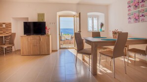 A modern kitchen with a television, wooden cabinets, and a dining area with chairs and a table. - Apartment Marija (Cres)