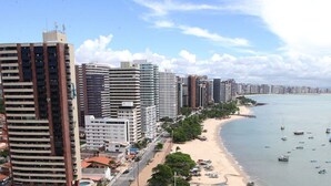 Un paisaje urbano costero con rascacielos, una playa de arena y numerosos barcos en el agua.
