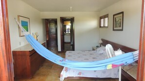 Un dormitorio con cama, cómoda de madera, escritorio, silla, ventilador y puerta que da a otra habitación.