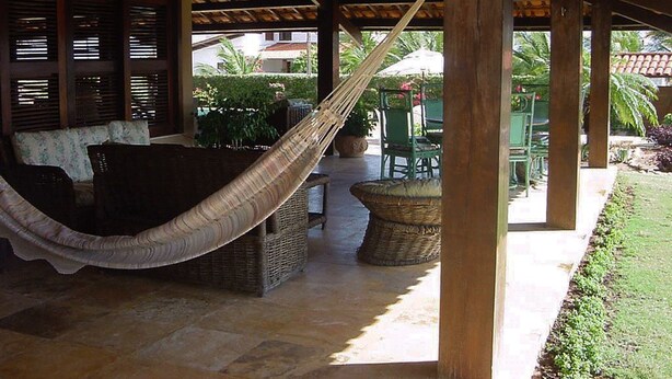 Un espacio al aire libre con techo, una hamaca, muebles de mimbre y vistas a la vegetación circundante.