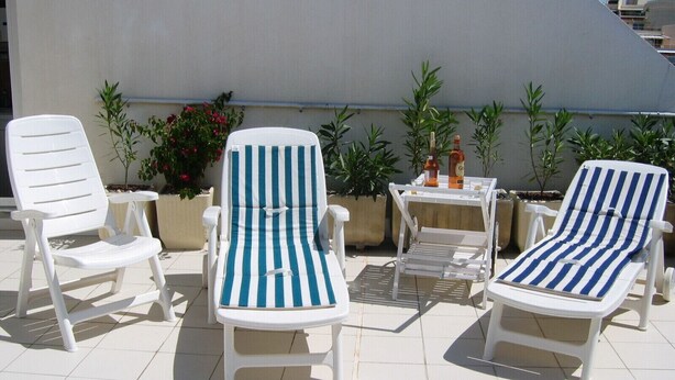 Two white lounge chairs with blue and white striped cushions, a small table with a bottle and glass, and potted plants against a white wall. - Very nice apartment. 5 rooms with terraces, 8 persons 150m. Beach (La Grande-Motte)