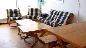 A cozy living room with striped sofas and wooden tables, a window with blinds, and a wall-mounted shelf with decorative items. - Very nice apartment. 5 rooms with terraces, 8 persons 150m. Beach (La Grande-Motte)