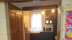A cozy living room with a sofa and a patterned throw pillow, leading to a kitchen with a sink, cabinets, and a microwave.