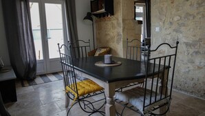 A dining area with a stone wall, a table with four chairs, a candle on the table, and a door leading outside.