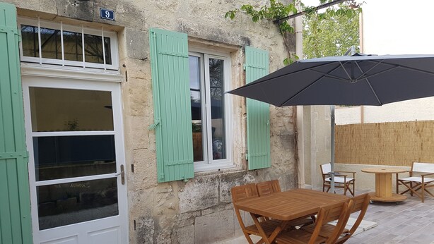 A rustic outdoor patio with a wooden table and chairs, a black umbrella, and a wooden fence.