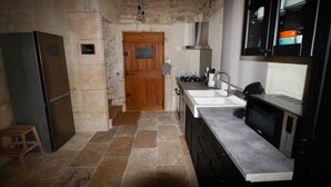 A kitchen with a stone wall, a wooden door, a stainless steel refrigerator, a sink, and a microwave.