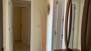 Een gang met een spiegel, een decoratieve plant en een deur naar een andere kamer.