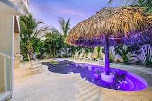 A pool area with a thatched umbrella, lounge chairs, and tropical plants.