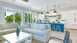 A spacious living area with a sofa, a coffee table, and a blue chair. There is a kitchen with blue bar stools and white cabinets. - Beach Views - Family-Friendly, Steps to Lido Beach! (Lido Key)