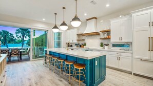 A modern kitchen with a large island, bar stools, white cabinets, and a view of the outdoors. - Beach Views - Family-Friendly, Steps to Lido Beach! (Lido Key)