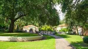 A well-maintained garden with a curved pathway, a large tree, and a building with a tiled roof. - Your Orlando theme park and shopping paradise!       Long term renters welcome (Kissimmee)