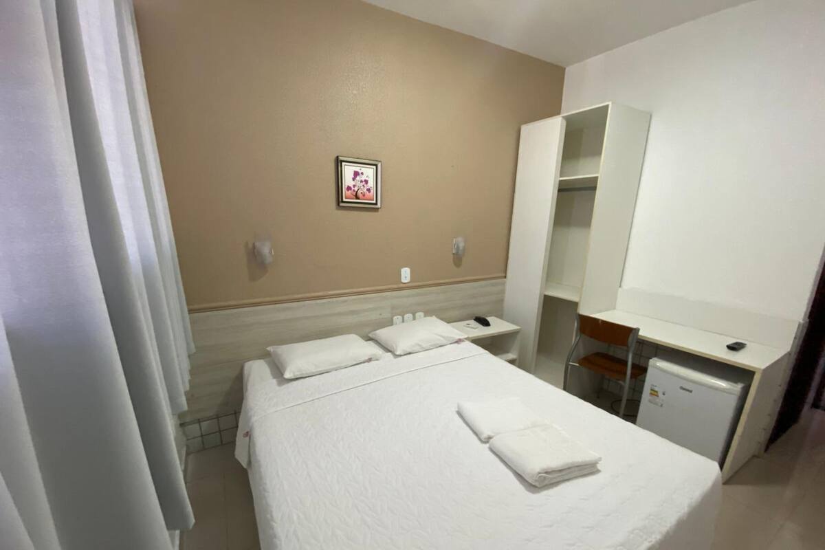 Ett hotellrum med en säng, ett skrivbord, en spegel och ett litet kylskåp.