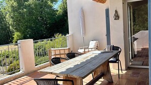 Une terrasse extérieure avec une table et des chaises en bois, une pergola agrémentée de guirlandes lumineuses et une vue sur la verdure.