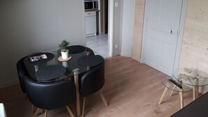 A compact dining area with a glass table, black chairs, and a small potted plant. A microwave is visible in the adjacent kitchen area. - Waterfront apartment with your feet in the water! (Langrune-sur-Mer)