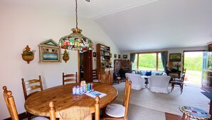 En matplats med ett runt träbord, omgivet av trästolar med vadderade sitsar. Ovanför bordet hänger en lampa med en dekorativ skärm av färgat glas.