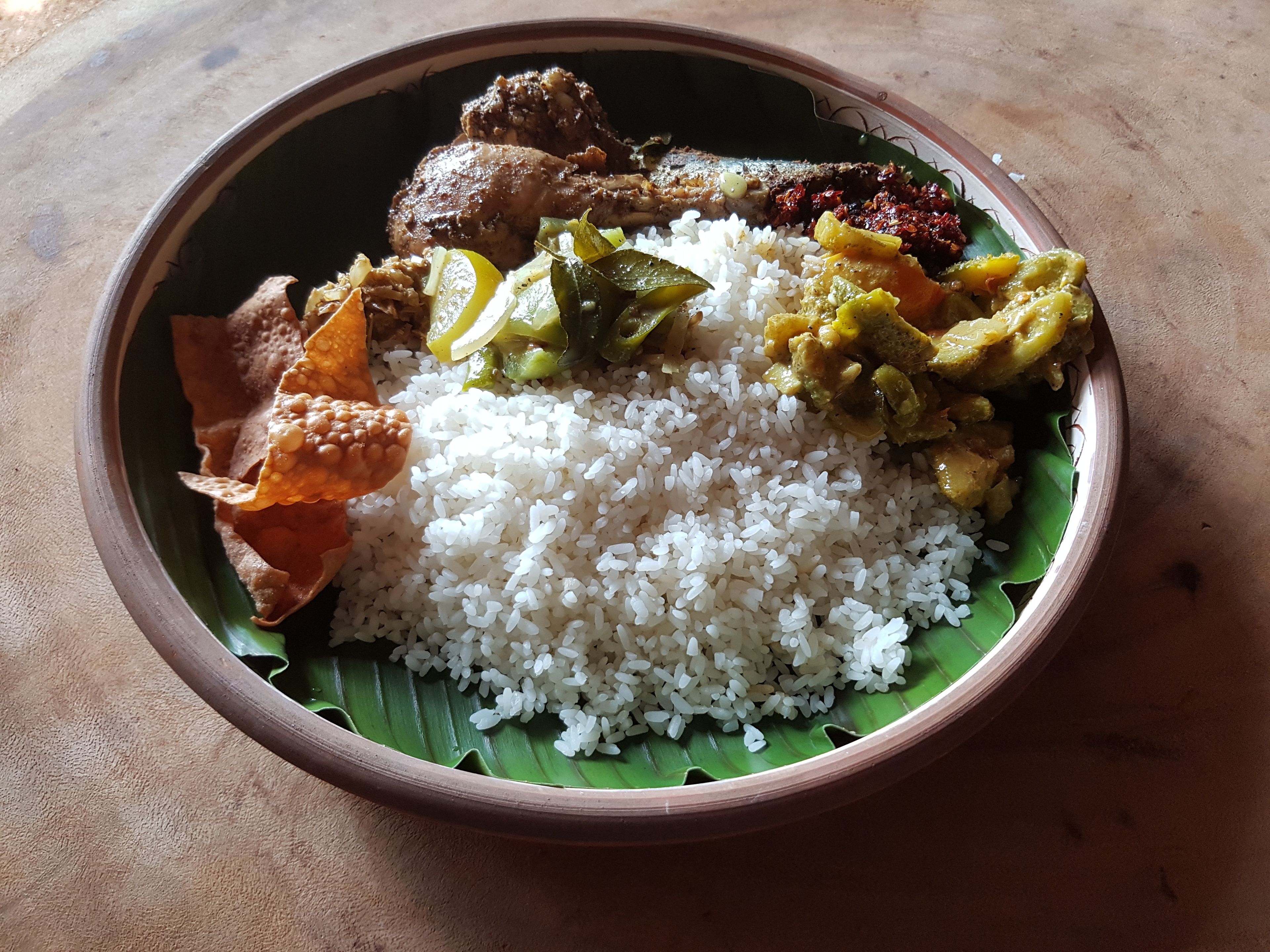 A meal served on a banana leaf with white rice, chicken, and various vegetable dishes.