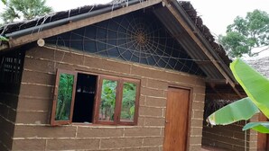 Una casa rústica con techo de paja, puerta de madera y ventana con contraventanas abiertas.
