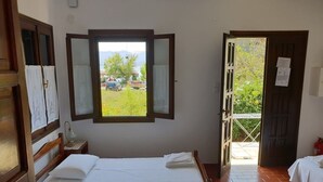 A room with two beds, a window with a view of greenery and parked cars, and a door leading to an outdoor area. - Zmas Studios (South Pelion)