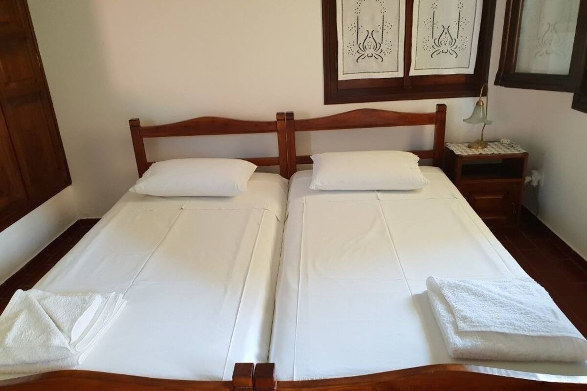 A double bed with white linens and two pillows, a wooden headboard, a bedside table with a lamp, and framed artwork on the wall.